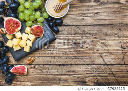 Cheese cubes, fresh fruit figs grapes Honey walnut on wooden chopping Board. Copy space. 57922325