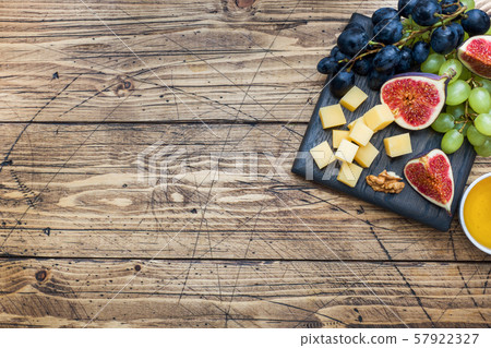 Cheese cubes, fresh fruit figs grapes Honey walnut on wooden chopping Board. Copy space. 57922327