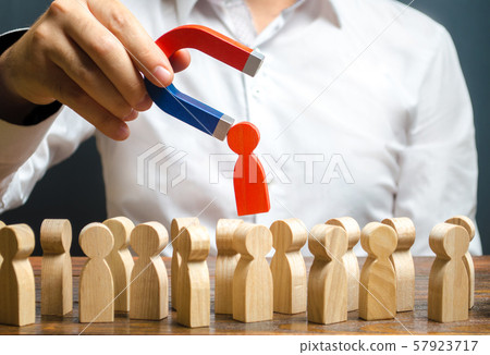 A hand with a magnet pulls red human figure out of the big crowd of people. Recruiting new workers, headhunters. Search for talented worker. demand for specialists. qualities skills of candidate A hand with a magnet pulls red human figure out of the big crowd of people. Recruiting new workers, headhunters. Search for talented worker. demand for specialists. qualities skills of candidate 57923717