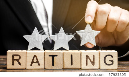 Businessman puts the third star above the word Rating on wooden blocks. The concept of quality of service. Hotel or restaurant rating. Evaluation of critics and visitors. Good quality. Feedback. Three 57923805