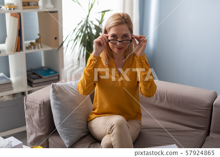 Smiling female psychologist looking over eyeglasses while sitting on sofa Smiling female psychologist looking over eyeglasses while sitting on sofa 57924865
