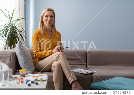 Smiling female psychologist holding eyeglasses in arms during art therapy seance Smiling female psychologist holding eyeglasses in arms during art therapy seance 57924875
