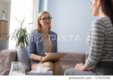 Low angle of psychologist in eyeglasses with clipboard listeting attentively to patient 57925096