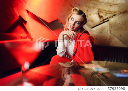 Photo of young blonde in red jacket looking up sitting on sofa at table 57927098