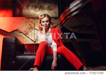 Full-lenght photo of blonde woman in red jacket sitting on leather sofa in nightclub 57927100