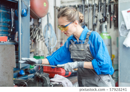 Woman worker in metal workshop deburring workpiece 57928241