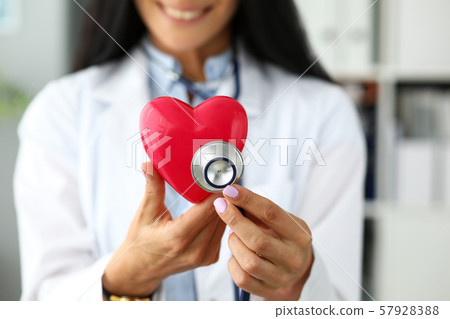 Hands of female GP holding stethoscope head near red toy heart Hands of female GP holding stethoscope head near red toy heart 57928388