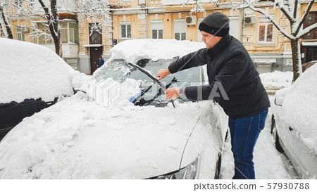 Shot of man in jacket trying to clean up car from snow with brush at frosty morning 57930788