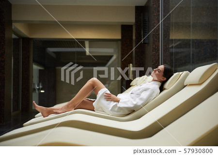 Attractive young woman in soft white bathrobe lying on comfortable daybed 57930800