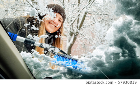 Closeup image inside the snow covered car. Beautiful young smiling woman in brown hat trying to 57930819