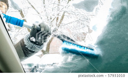 Close up image inside the snow covered car. Smiling lady clean up the windshield and wipers of her 57931010