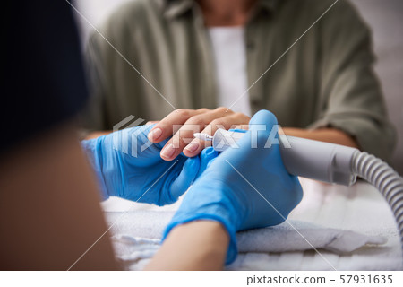 Manicurist removing cuticle on lady fingers with electric nail mill Manicurist removing cuticle on lady fingers with electric nail mill 57931635