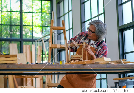 Old craftsman use sandpaper to scrub small building model in glass room with day light Old craftsman use sandpaper to scrub small building model in glass room with day light 57931651