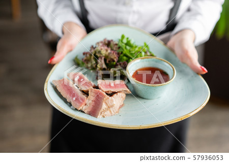 The waiter is holding a plate medium rare tuna with lettuce and hot sauce. Restaurant menu The waiter is holding a plate medium rare tuna with lettuce and hot sauce. Restaurant menu 57936053