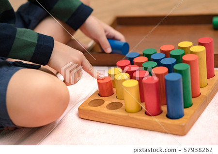 Closeup: Hands of a little Montessori kid (3-6) learning about size, orders, sorting, arranging by engaged colorful wooden sensorial blocks. Educational toys, Cognitive skills, Montessori activity.  57938262