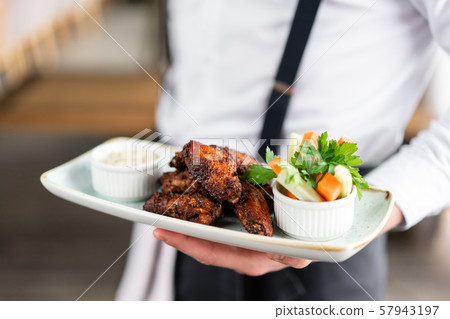 The waiter is holding a plate chicken wings grill. Barbecue restaurant menu, a series of photos of 57943197