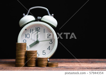 Alarm clock and coins stacks on working table in Alarm clock and coins stacks on working table in 57944354