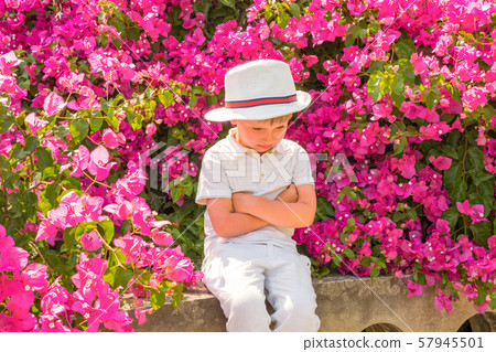 Sad boy with hands folded in front of him in white closed sitting in park. Offended boy in stylish Sad boy with hands folded in front of him in white closed sitting in park. Offended boy in stylish 57945501