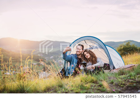 Young tourist couple travellers with tent shelter sitting in nature, taking selfie. Young tourist couple travellers with tent shelter sitting in nature, taking selfie. 57945545