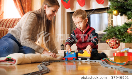 Portrait of boy with his mother playing on floor with toy train and railways. Child receiving Portrait of boy with his mother playing on floor with toy train and railways. Child receiving 57946901