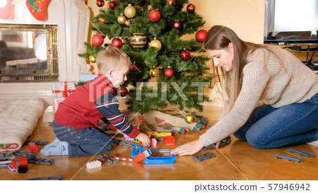 Portrait of happy smiling little boy with mother building railroad and playing with toy train on 57946942