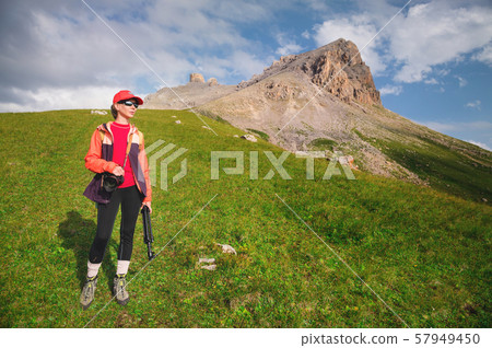 Girl athlete photographer in a red cap sunglasses and a yellow backpack stands on a green slope 57949450