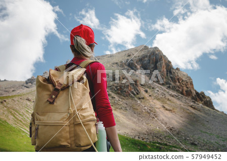 View from the back Girl athlete in a red cap sunglasses and a yellow backpack stands on a green 57949452