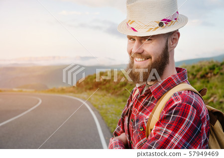 Portrait of a bearded happy smiling traveler hipster with a backpack in a plaid shirt and a hat next 57949469