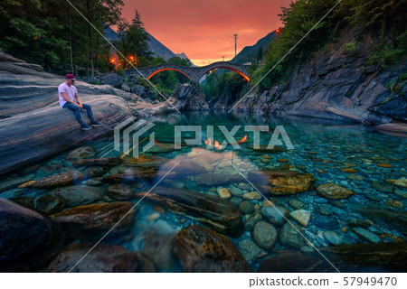 Tourist enjoys sunset at a river near stone bridge in Lavertezzo, Switzerland 57949470