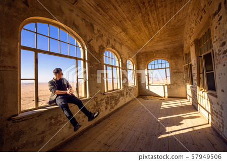 Tourist sits in a widow of a ruined house in Kolmanskop ghost town, Namibia 57949506