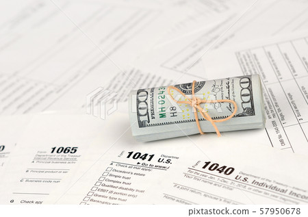 Tax forms lies near roll of hundred dollar bills. Tax forms lies near roll of hundred dollar bills. 57950678