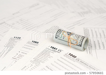 Tax forms lies near roll of hundred dollar bills. Tax forms lies near roll of hundred dollar bills. 57950681
