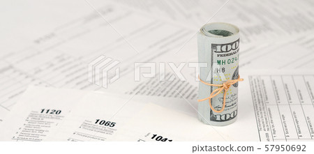 Tax forms lies near roll of hundred dollar bills. Tax forms lies near roll of hundred dollar bills. 57950692