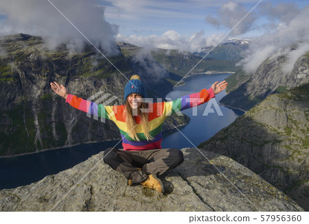 Girl sits on rock against blue lake and mountains Girl sits on rock against blue lake and mountains 57956360
