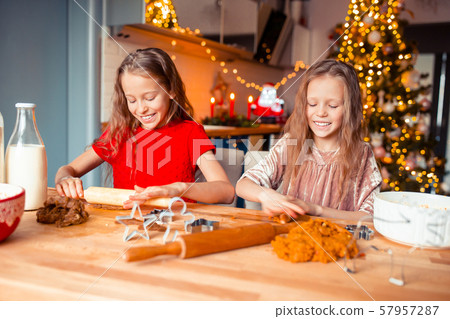 Little girls making Christmas gingerbread house at fireplace in decorated living room. Little girls making Christmas gingerbread house at fireplace in decorated living room. 57957287
