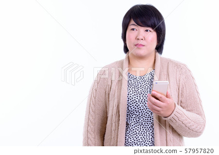 Beautiful overweight Asian woman thinking while using phone ready for winter 57957820
