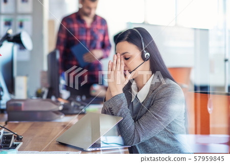 Tired young woman is sitting at the table at work in a call center. 57959845