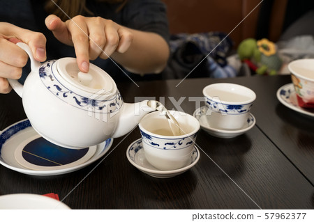 Teapot in the hands of a girl pouring green tea into beautiful chinese cups Teapot in the hands of a girl pouring green tea into beautiful chinese cups 57962377