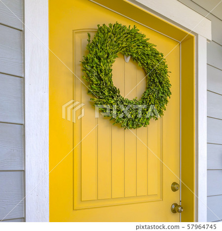 Yellow front door with ornamental green wreath 57964745