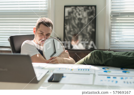 Tired young man sits sad at the desk and hugs the 57969167
