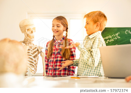 Pleased blonde kids looking at artificial skeleton Pleased blonde kids looking at artificial skeleton 57972374