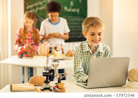 Positive delighted blonde boy staring at computer Positive delighted blonde boy staring at computer 57972546