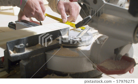 Hands of carpenter measuring a wooden plank Hands of carpenter measuring a wooden plank 57976275