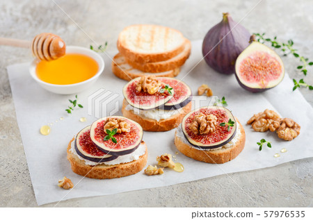 Bruschetta with fresh ricotta cheese, figs, nuts, thyme and honey on gray concrete background. Bruschetta with fresh ricotta cheese, figs, nuts, thyme and honey on gray concrete background. 57976535