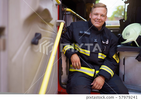 Photo of smiling fireman sitting in fire truck at fire station 57979241