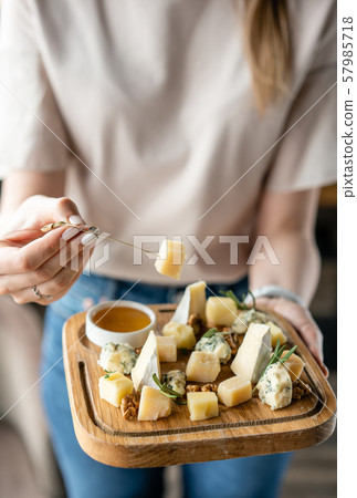 Girl holding piece of parmesan cheese on a skewer and wooden plate with cheese. Delicious cheese mix Girl holding piece of parmesan cheese on a skewer and wooden plate with cheese. Delicious cheese mix 57985718