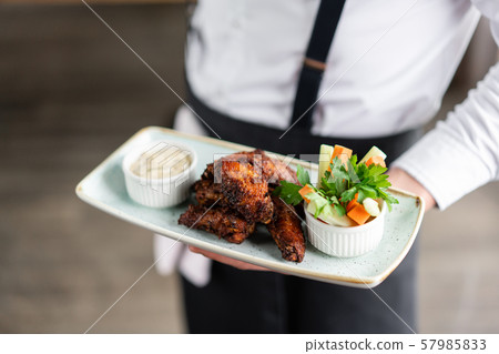 The waiter is holding a plate chicken wings grill. Barbecue restaurant menu, a series of photos of 57985833