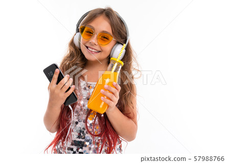 Smiling girl wearing glittery dress and bright yellow sunglasses, with big white earphones 57988766