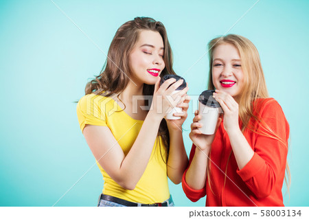Two smiling girls have coffee time on blue Two smiling girls have coffee time on blue 58003134