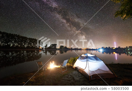 Tourist tent, two camping chairs and campfire on lake shore at night Tourist tent, two camping chairs and campfire on lake shore at night 58003500